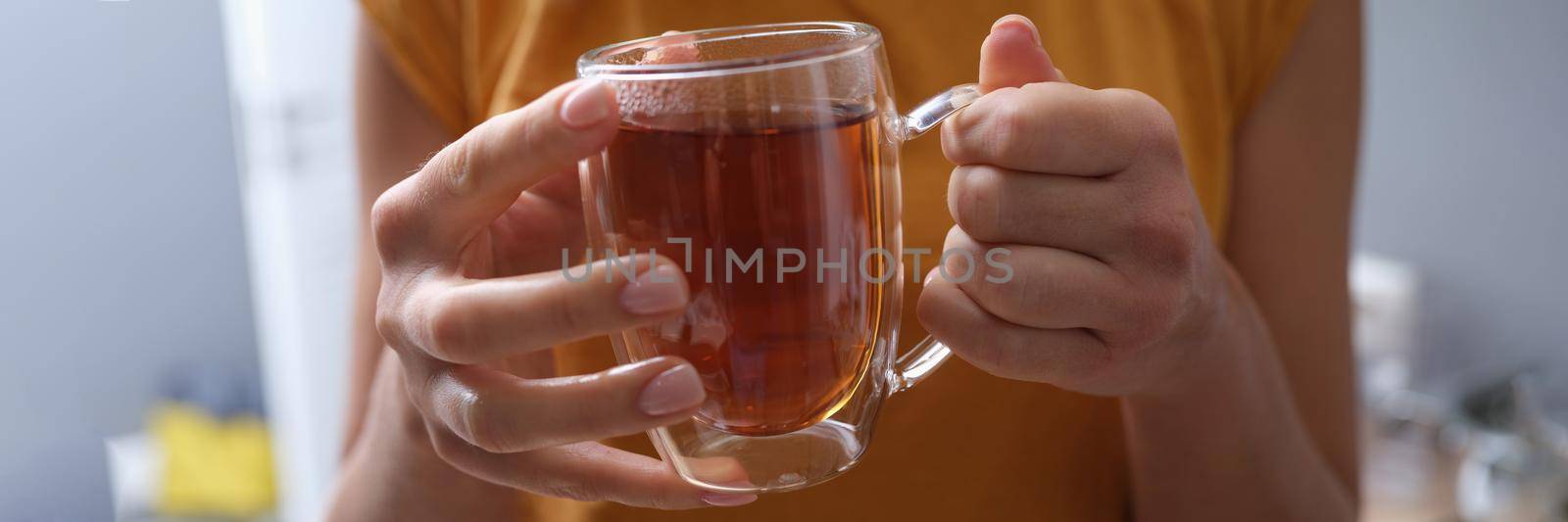 Woman holds transparent cup of hot tea in hands closeup by kuprevich