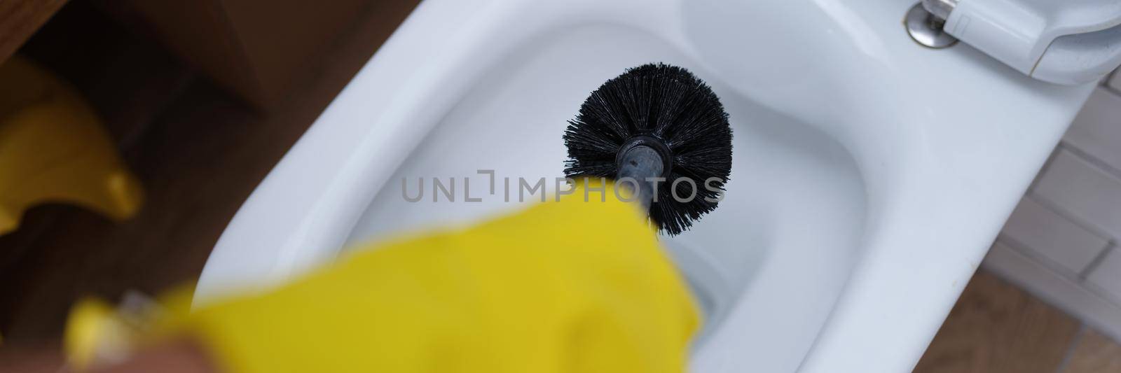 Hand in glove is cleaning toilet bowl with black brush closeup by kuprevich