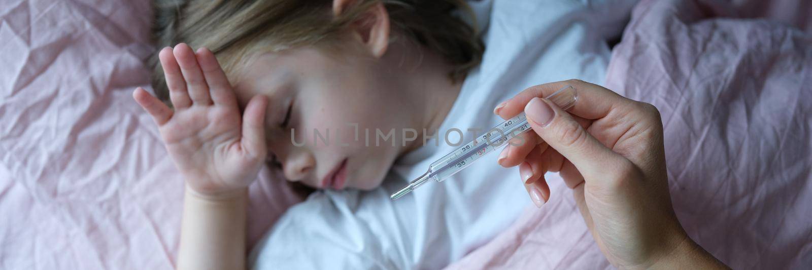 Mom measures body temperature of little sick girl lying in bed. Temporary increase in body temperature in a child