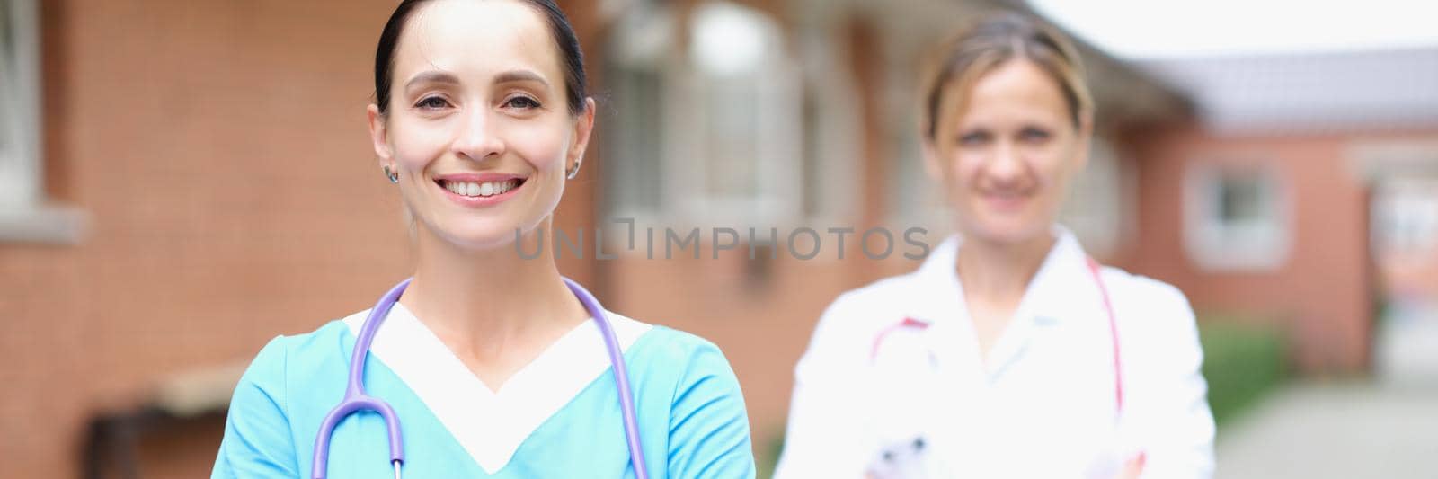 Two smiling female doctors stand with folded arms. Medical team concept