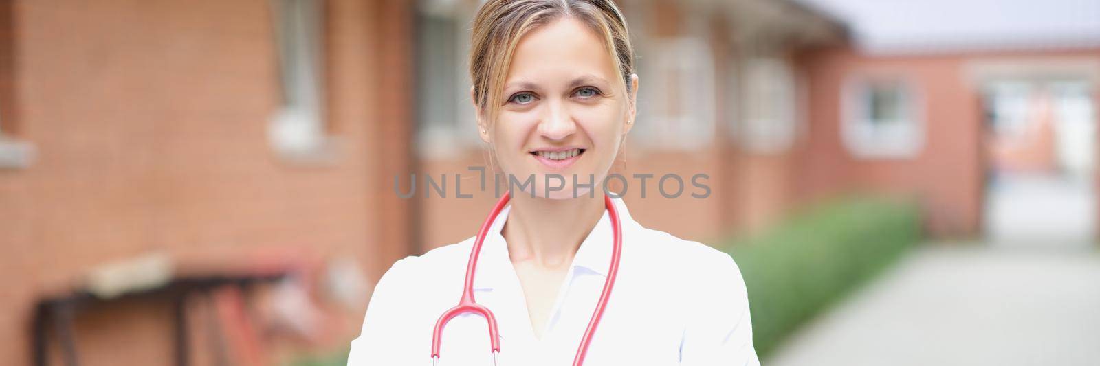 Portrait of a smiling female doctor with folded arms on street by kuprevich