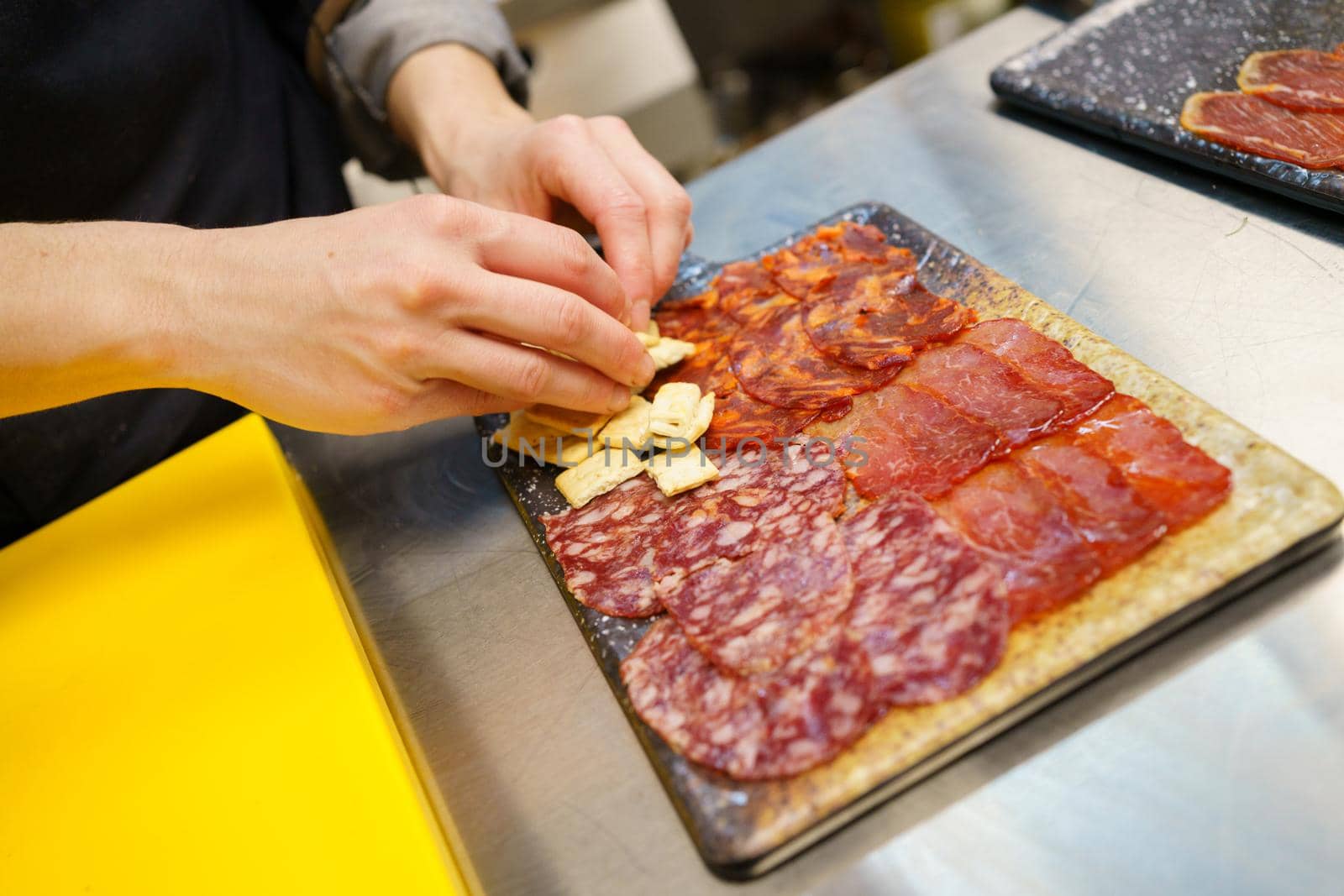 Unrecognizable chef preparing a plate of Iberian cured meats platter. A typical dish of Spanish cuisine. with crackers placed on board.