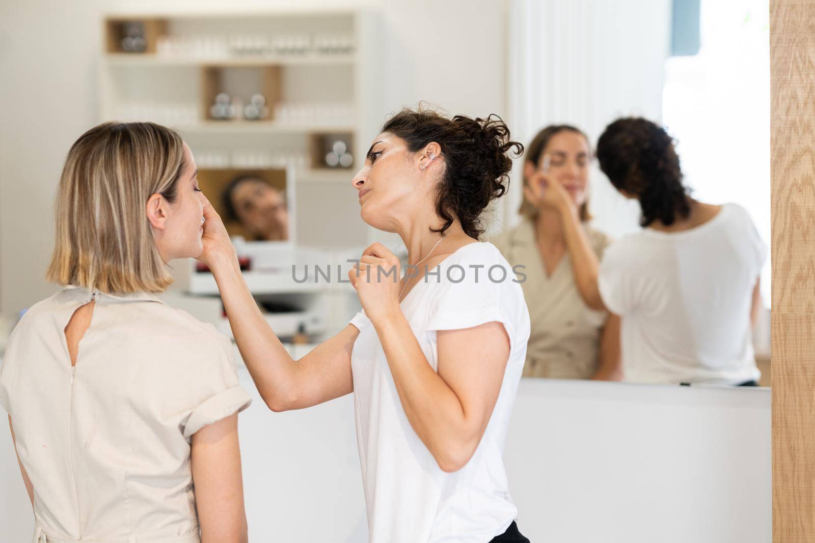 Professional female beautician doing skincare treatment on face of woman in modern beauty center