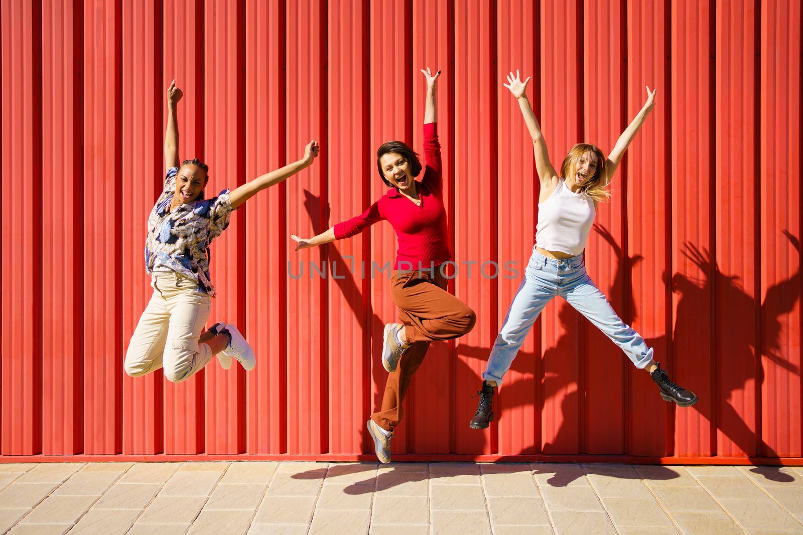 Cheerful diverse women jumping near wall by javiindy