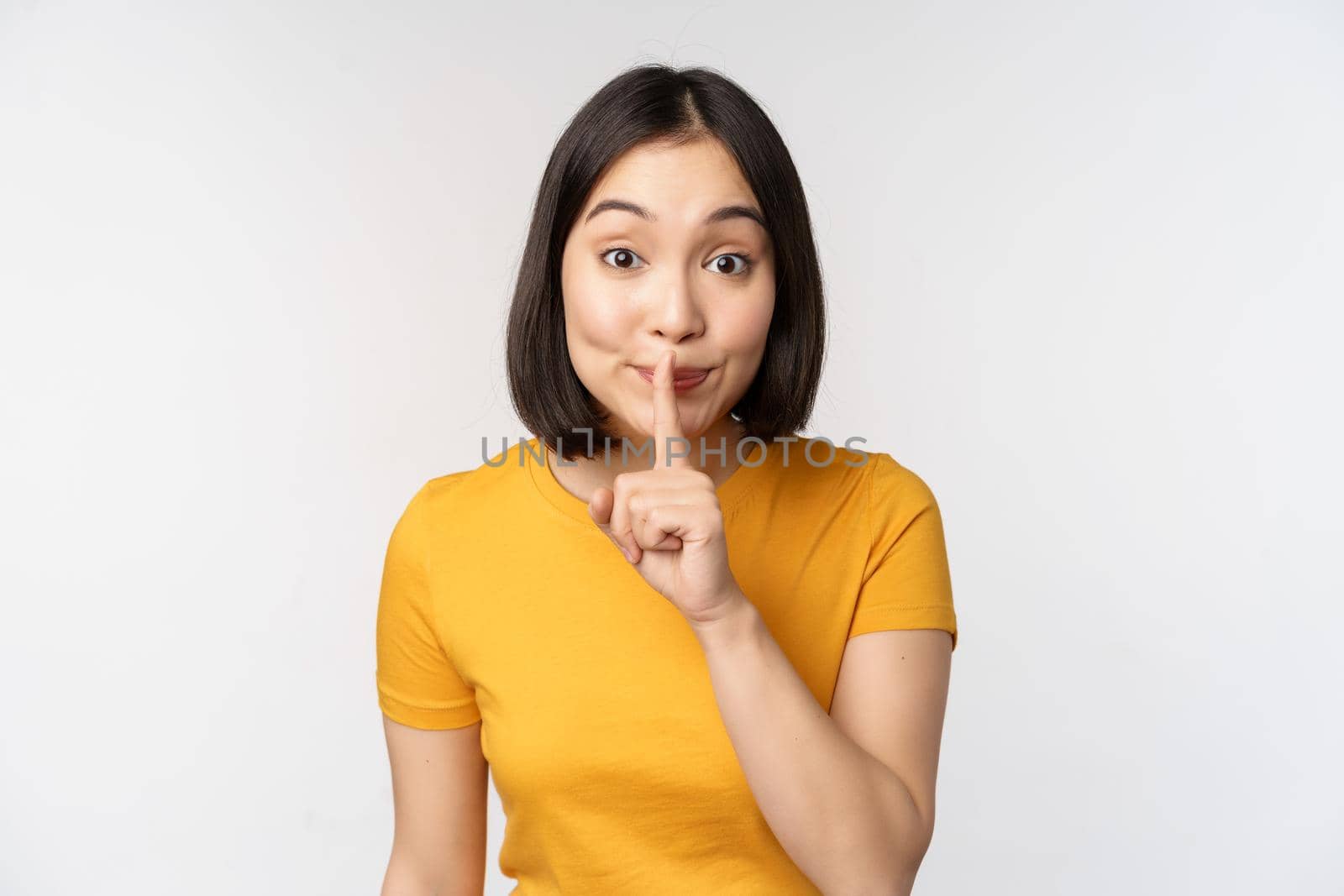 Keep quiet. Cute asian woman make shhh gest, showing shush, hush sign, press finger to lips, silence, standing over white background.