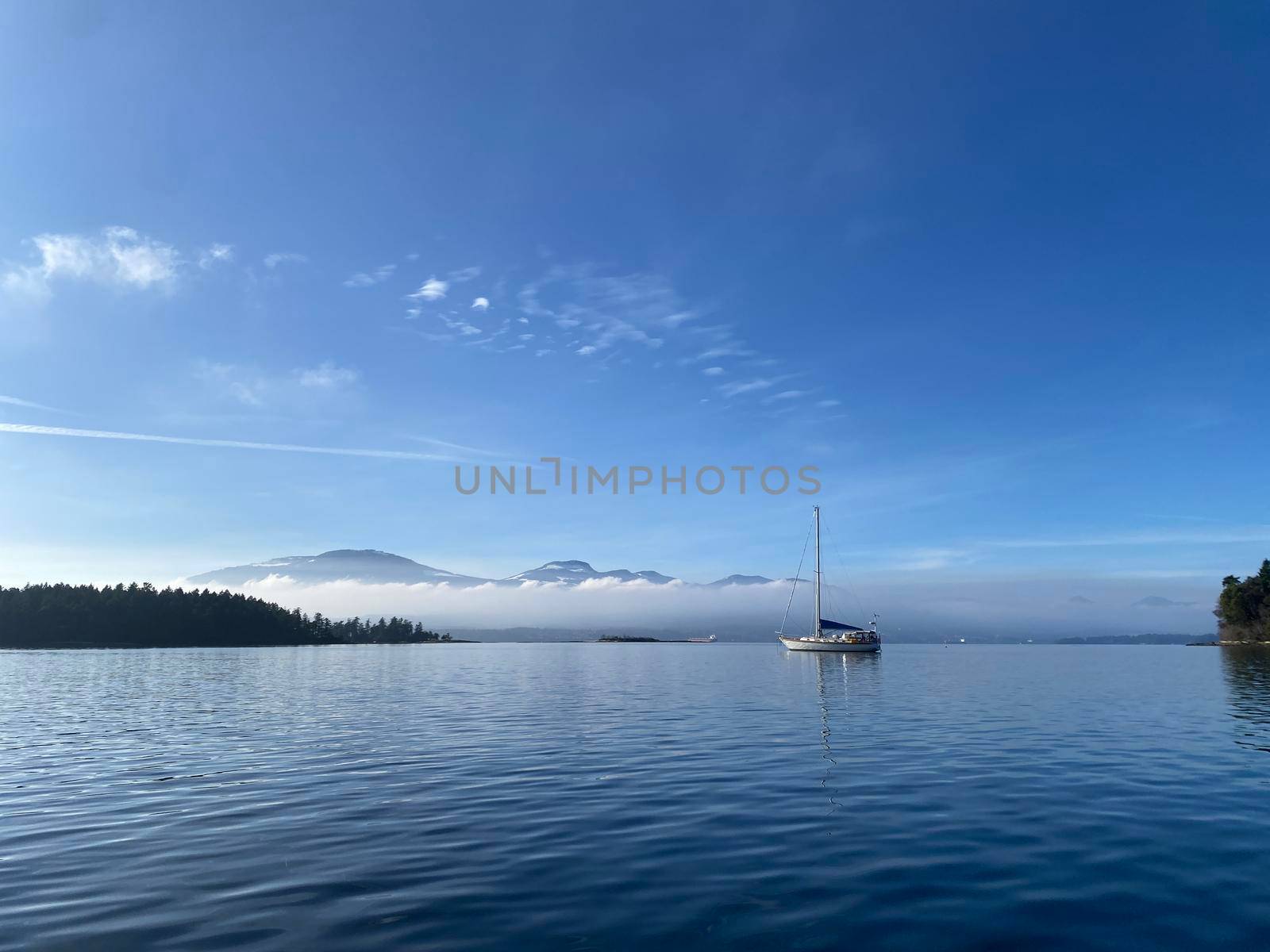 A single sailboat at anchor with calm water and blue skies by Granchinho