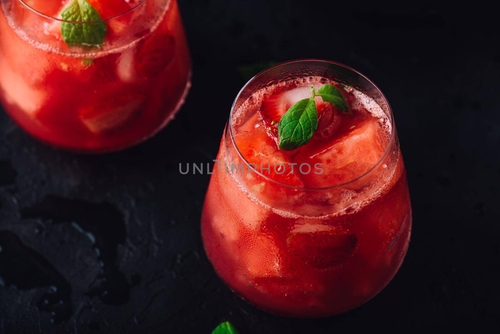 Glasses of cool watermelon and strawberry cocktail with mint garnish on dark concrete background