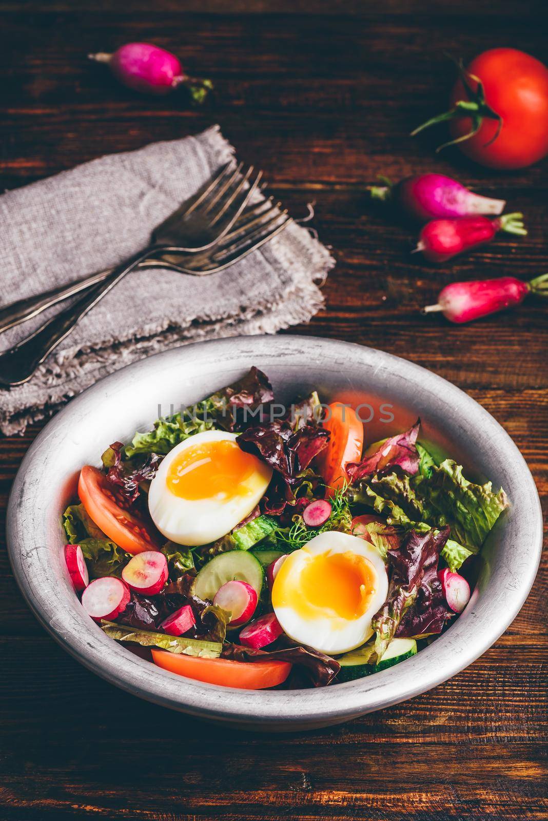 Fresh spring salad with tomato, radish, cucumber, red leaf lettuce and boiled eggs in metal bowl