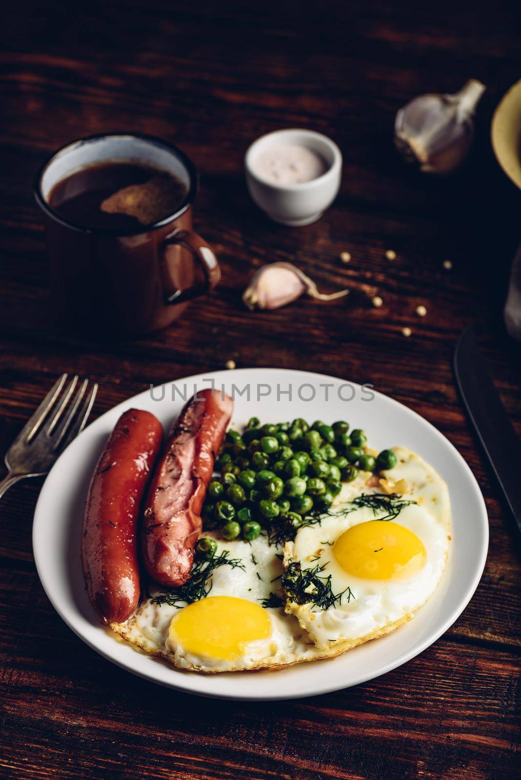 Breakfast with fried eggs, sausages and green peas on white plate