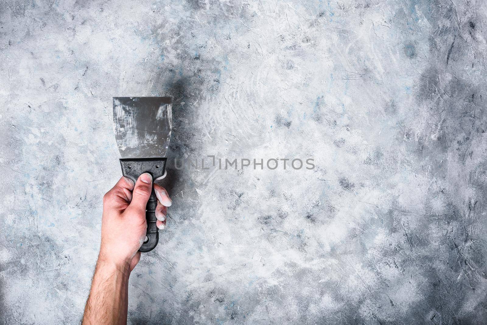 Hand holds dirty spatula. Gray concrete wall background.