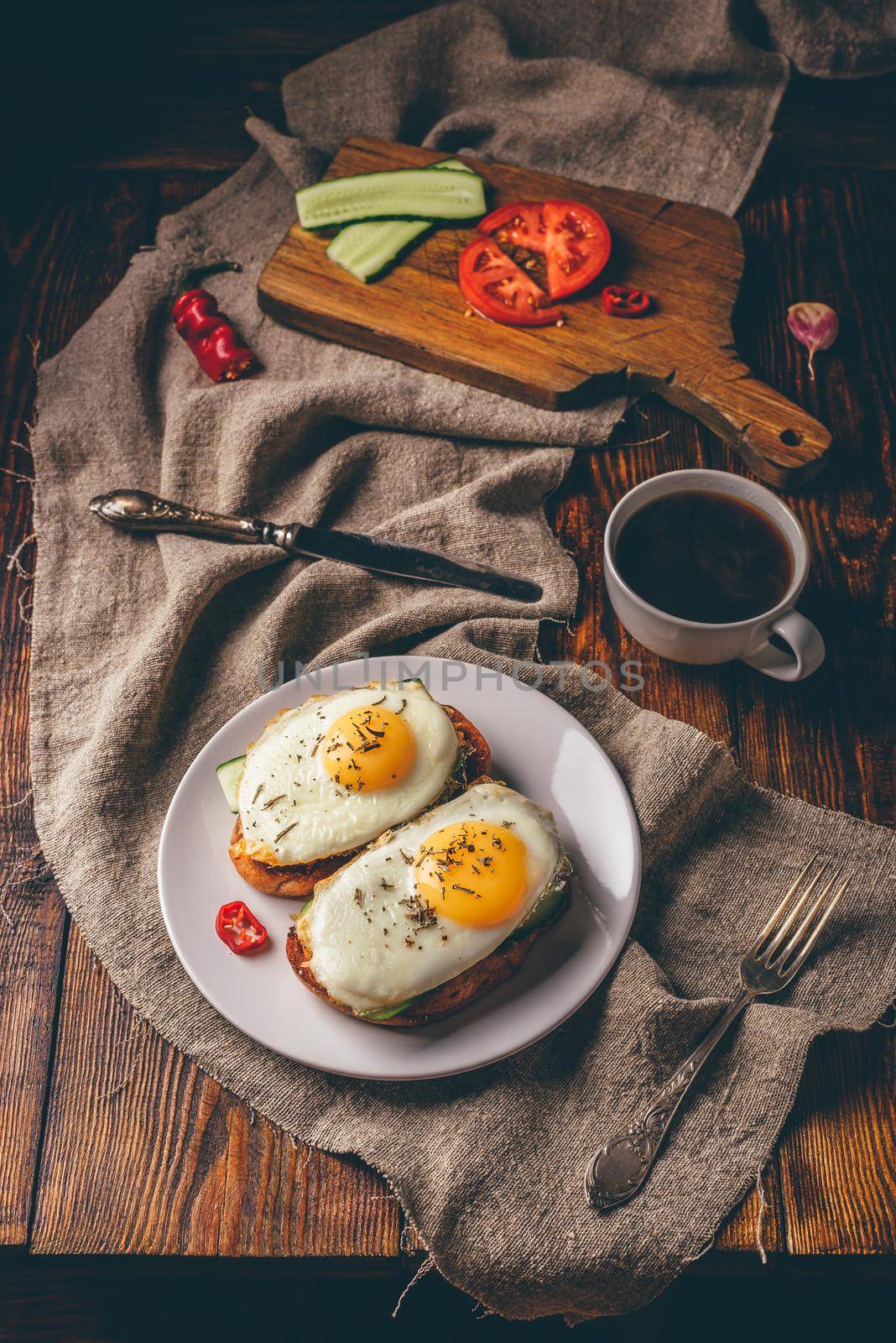 Breakfast toasts with vegetables and fried eggs on white plate and cup of coffee over grey rough cloth. Healthy food concept.