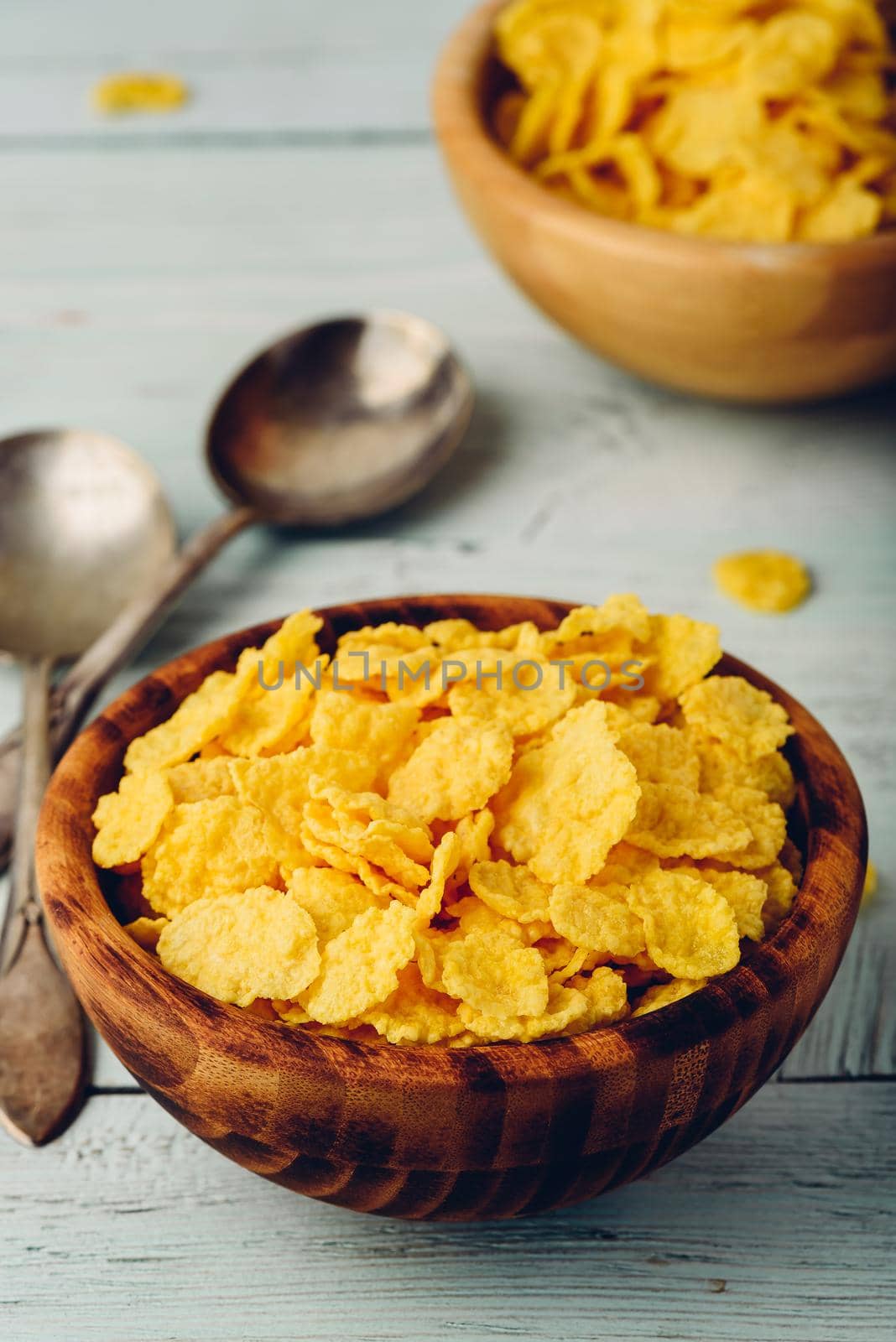 Rustic bowls of cornflakes with spoons on light wooden surface