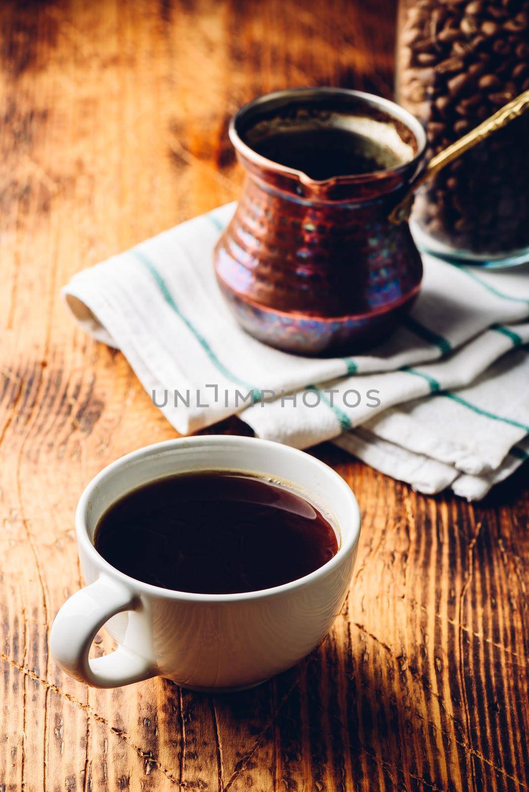 Cup of black coffee with copper cezve and jar of roasted coffee beans on wooden table