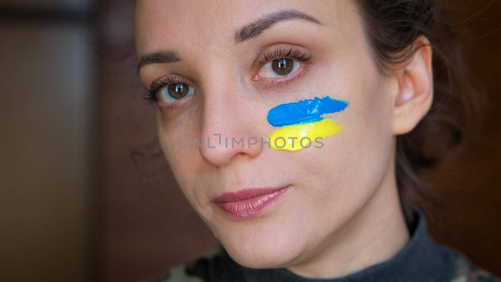 Indoor portrait of young girl with blue and yellow ukrainian flag on her cheek wearing military uniform, mandatory conscription in Ukraine, equality concepts by balinska_lv