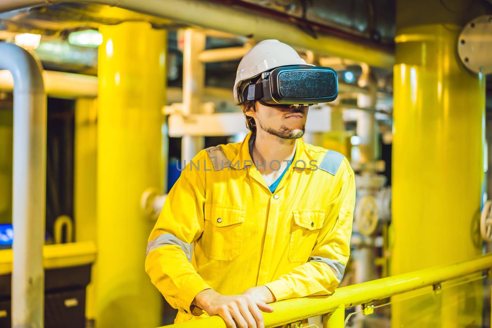 Young woman in a yellow work uniform, glasses and helmet uses virtual reality glasses in industrial environment,oil Platform or liquefied gas plant.