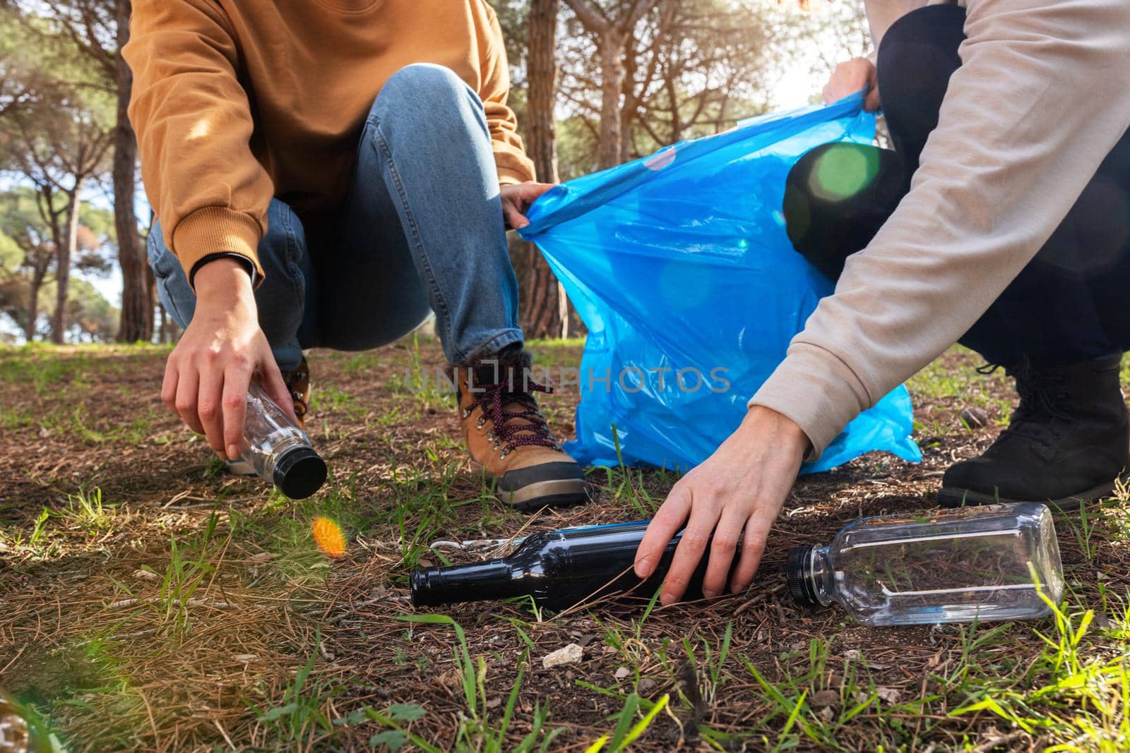 Unrecognizable people cleaning forest from plastic garbage and glass bottles. by Hoverstock