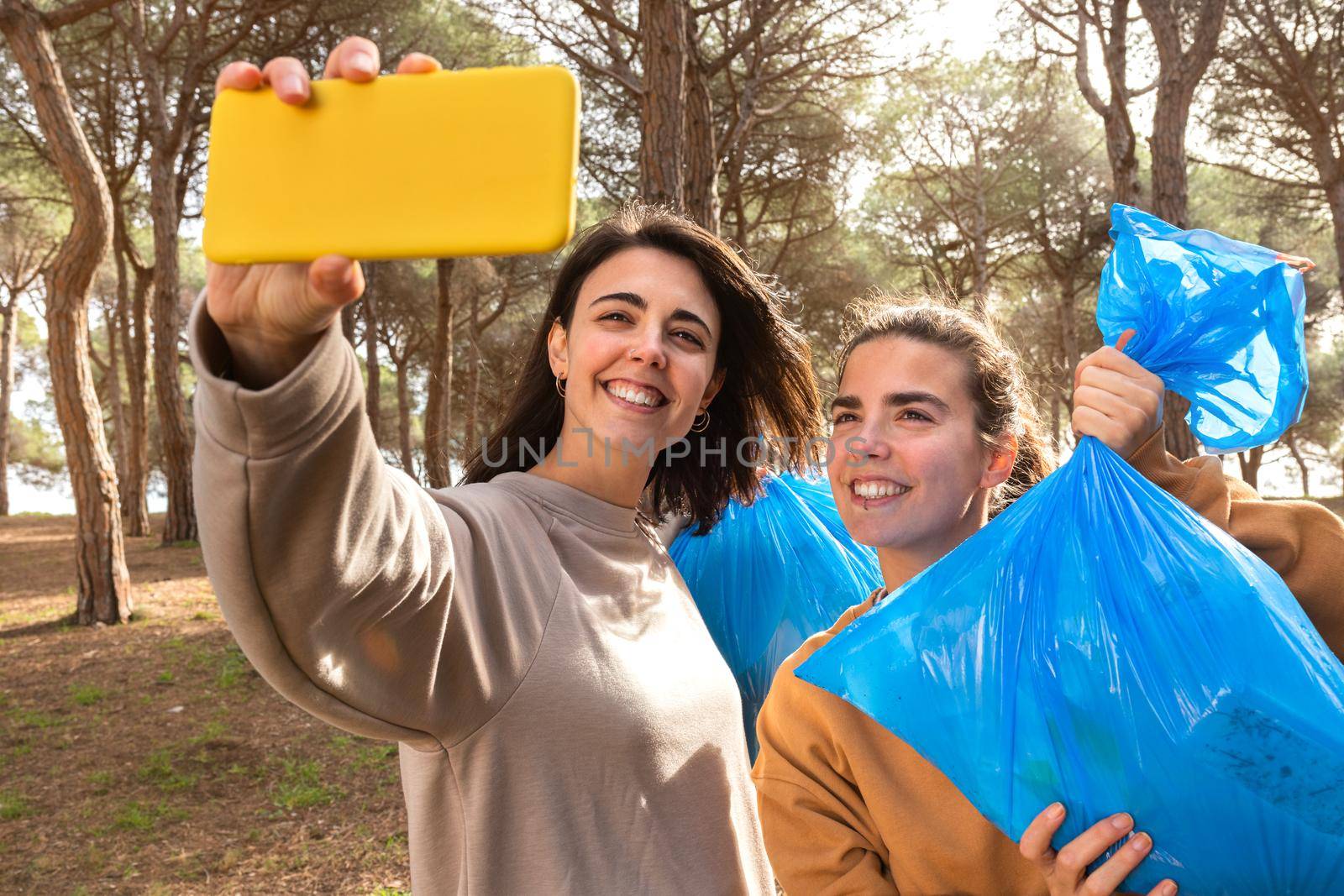 Young caucasian women take selfie with full garbage bags after cleaning the forest. Social media and environmentalism activist concept.