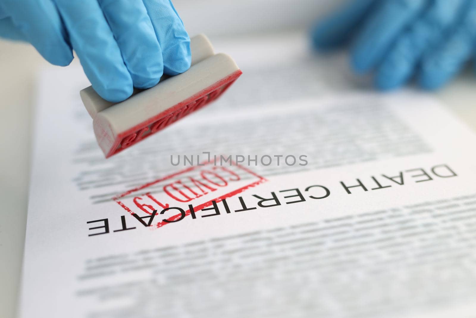 Pathologist putting red covid19 stamp on death certificate closeup by kuprevich