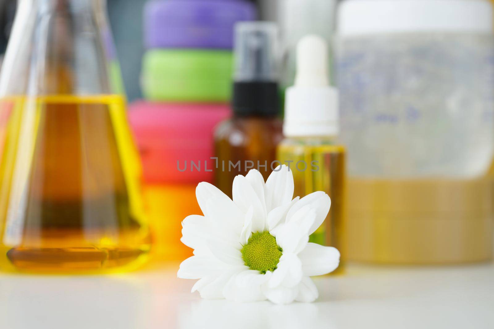 Close-up of chamomile flower and bottles with oils and other cosmetology products on background. Flasks with skincare, wellness. Body and face care concept