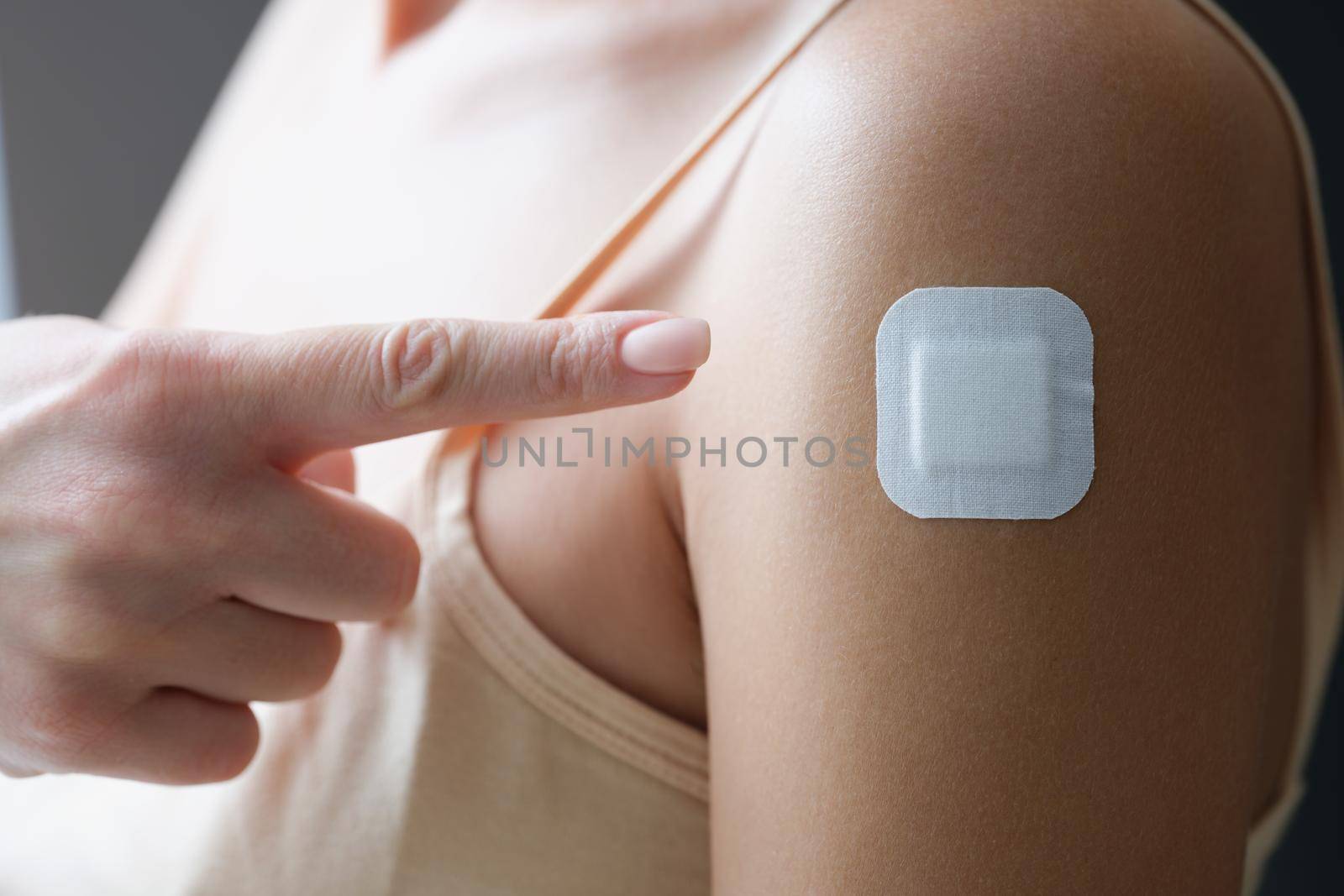 Close-up of woman point with finger at patch on arm, lady get vaccine. Bandage after scratch or injection of vaccine. Vaccination, medicine, health concept