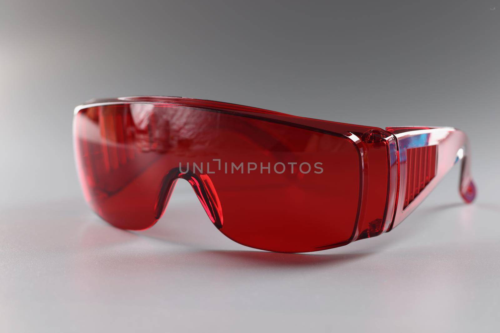 Close-up of red plastic safety glasses, protective workwear glasses for foreman worker. Reusable eyewear on grey background. Occupational safety concept