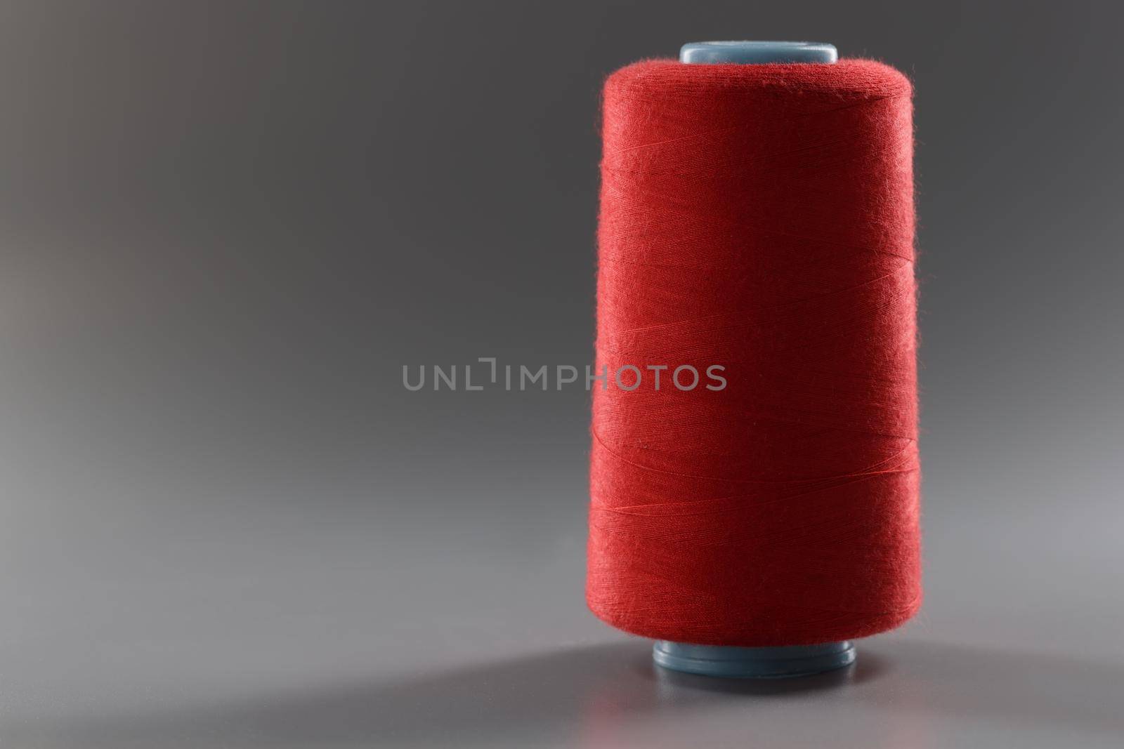 Red colour thread spool on grey background, yarn for sewing, bright thread for dressmaking by kuprevich