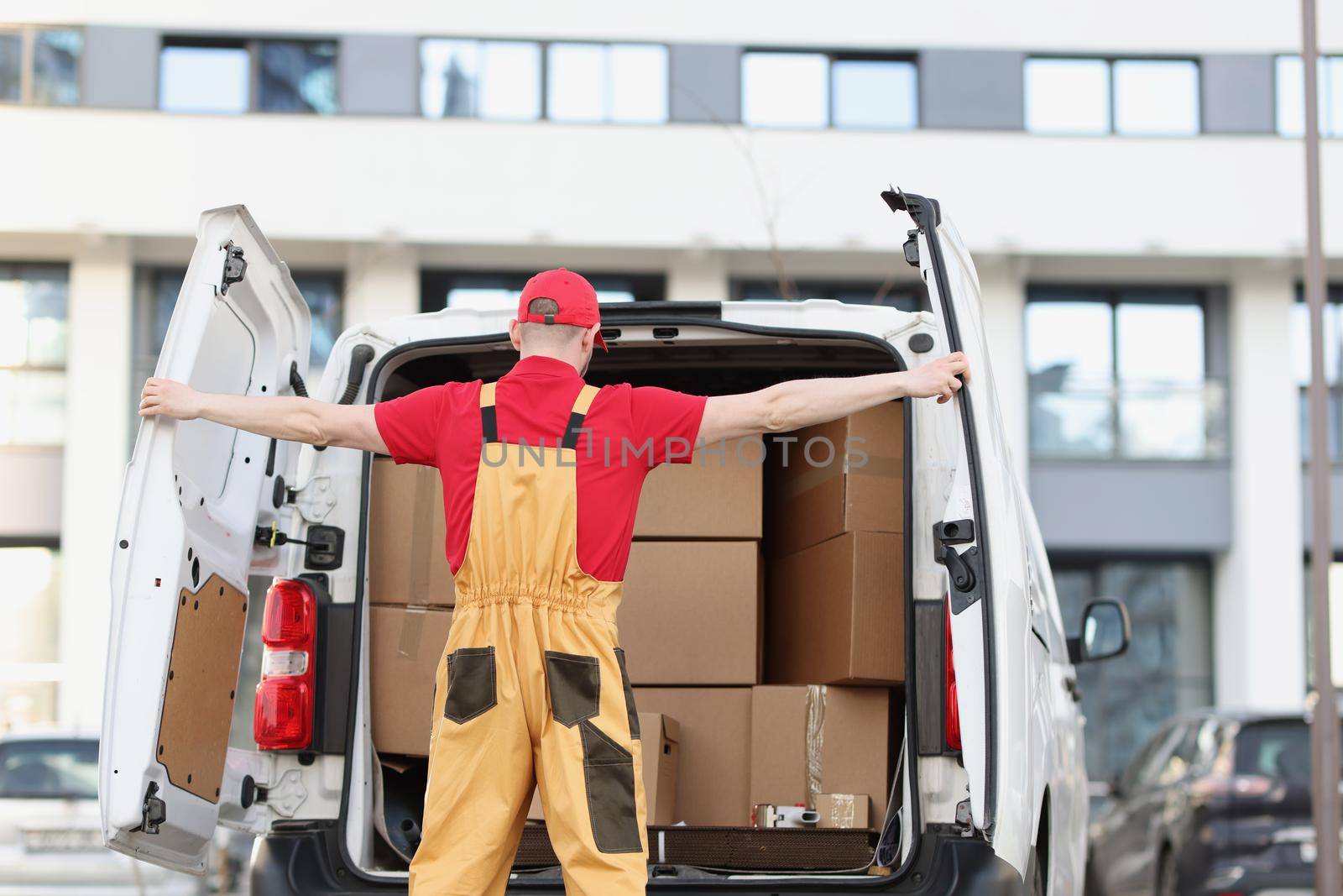 Portrait of person courier closing car door with both hands, view from back. Courier man in corporate uniform loaded boxes for delivery. Delivery concept