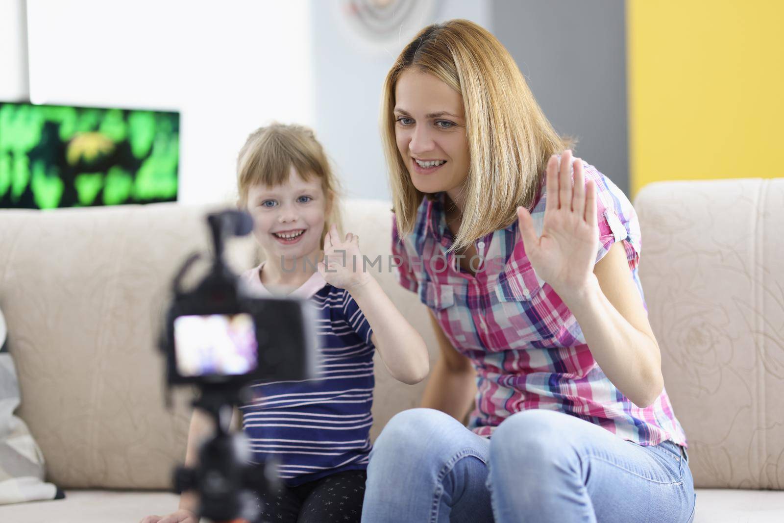 Mother and daughter wave hello and smile on camera, device record on tripod by kuprevich