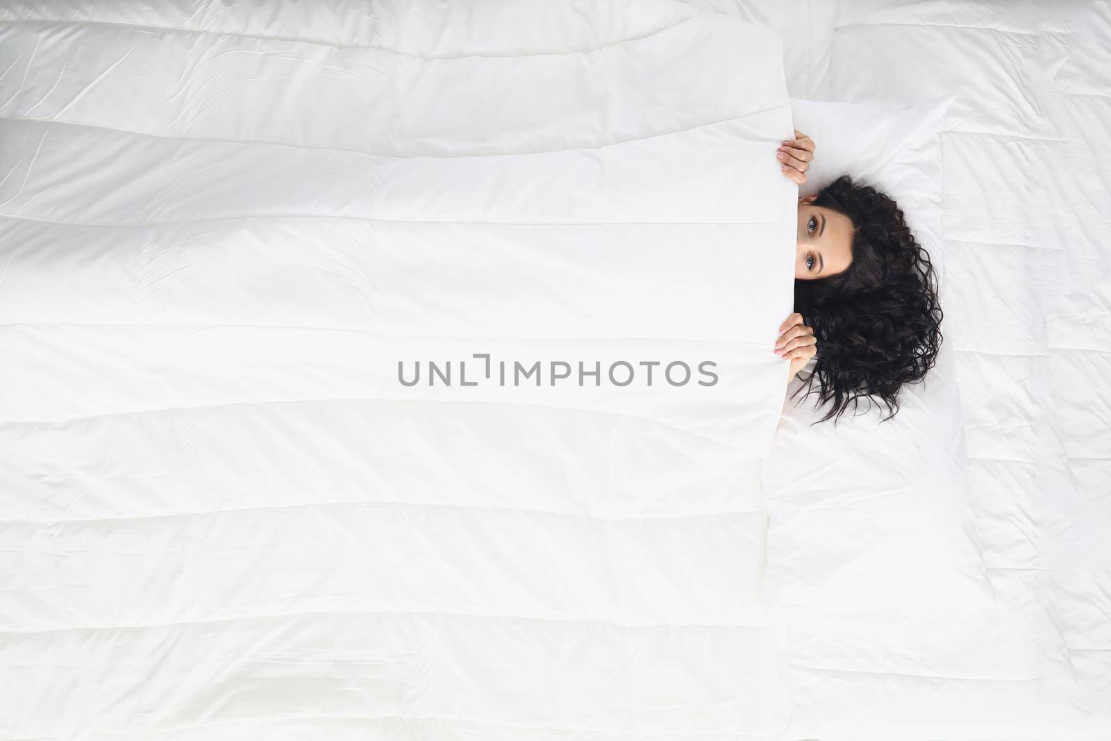 Woman laying on white bedding covering with blanket, wake up well rested in morning by kuprevich