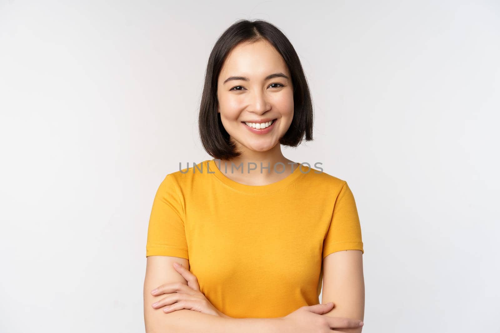 Portrait of young beautiful brunette, asian girl smiling and looking happy, cross arms on chest, standing over white background by Benzoix