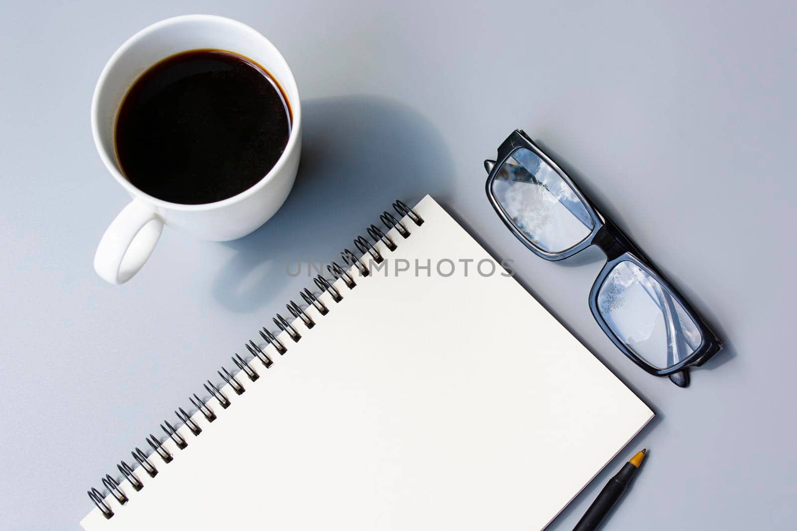 Notepad with cup of coffee and reading glasses on a desk. Directly above. Flat lay. For text usage