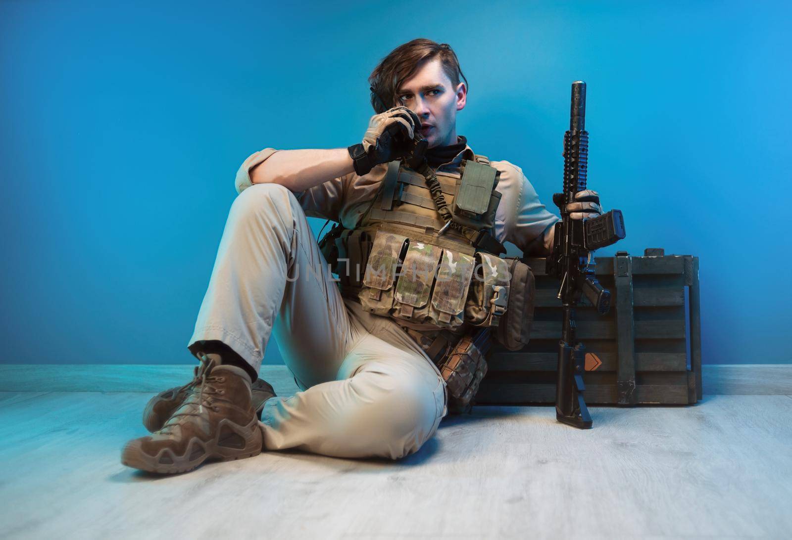 male soldier in camouflage is sitting by an ammunition crate on the floor with a weapon