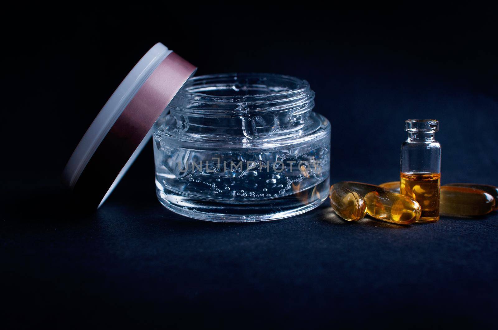 Transparent jar with cosmetic moisturizing gel with hyaluronic acid with bubbles and vitamins in capsules on a black background 