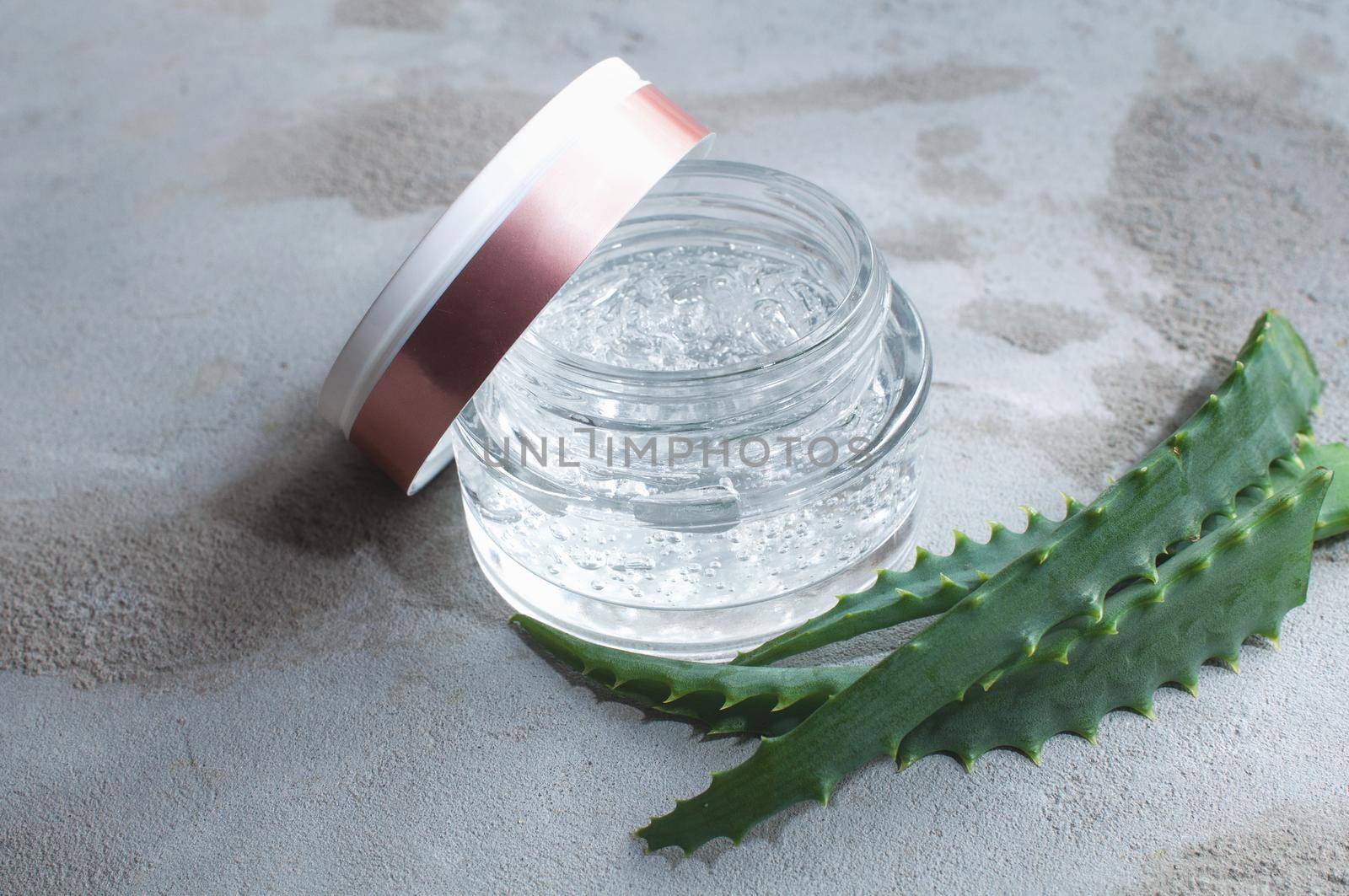 Gel texture with bubbles hyaluronic acid and aloe vera branches in a glass jar on a concrete background