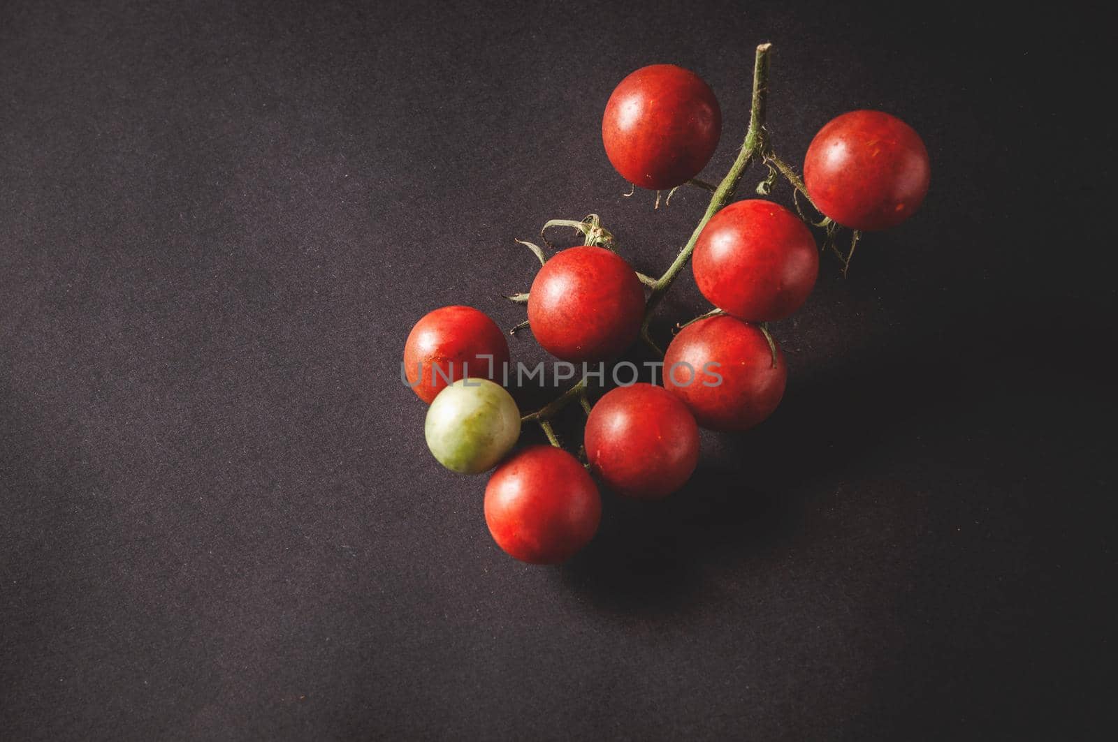 bunch of fresh cherry tomatoes on a branch are located on a black serving board on a dark background