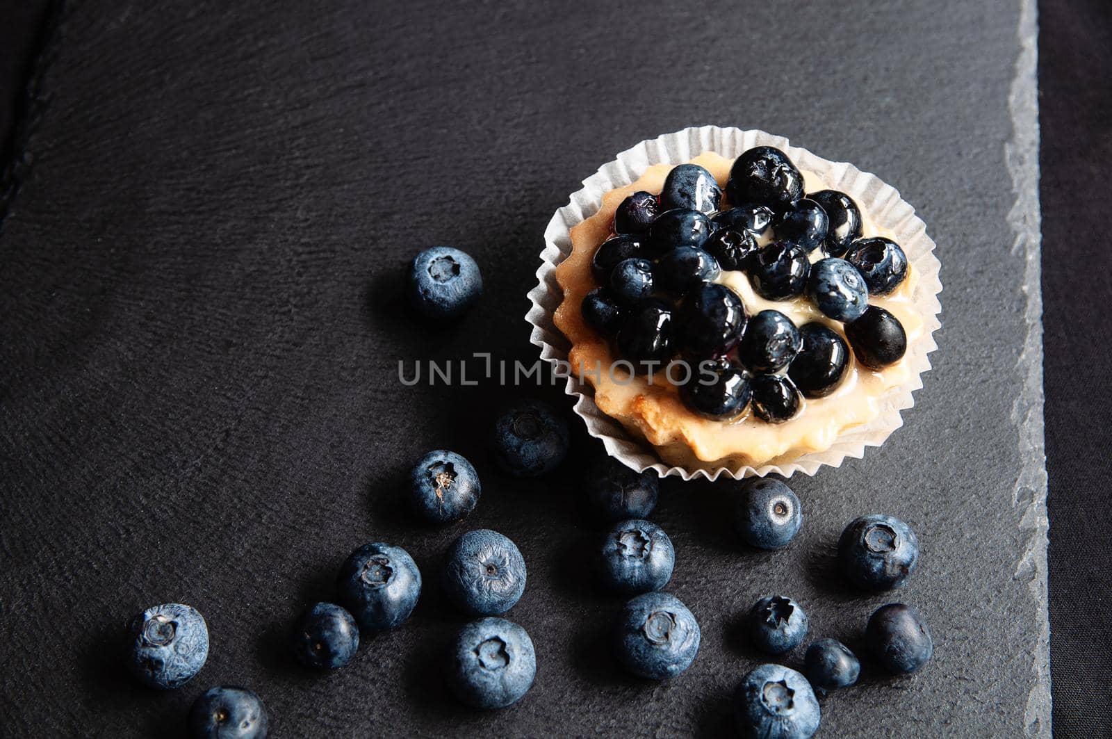 Tart with blueberries is on a black background of natural stone. by ozornina