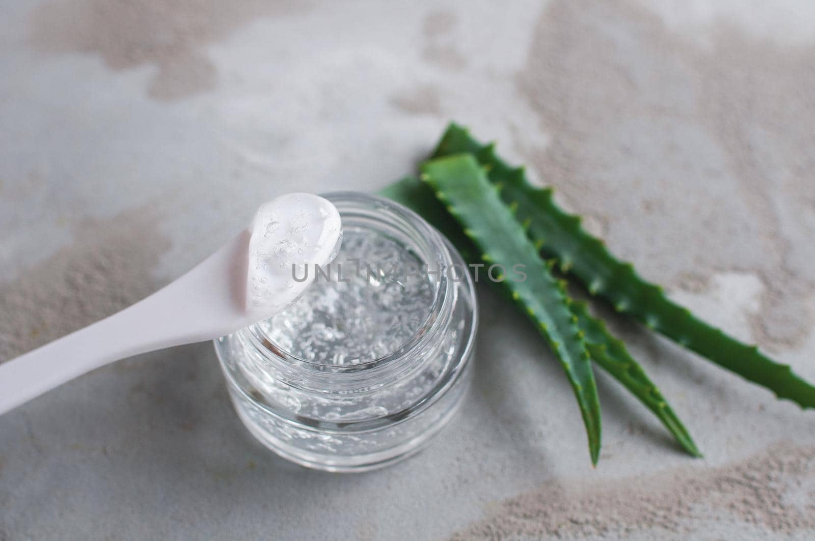 Gel with hyaluronic acid and aloe vera branches in a glass jar on a concrete background
