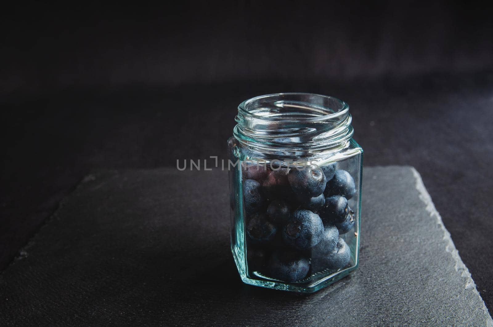 Fresh blueberries in a glass jar and laid out on a black board. Blueberries for a healthy diet and vegetarians
