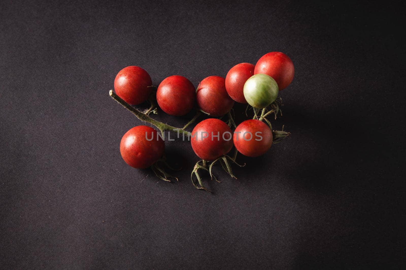 bunch of fresh cherry tomatoes on a branch are located on a black serving board  by ozornina