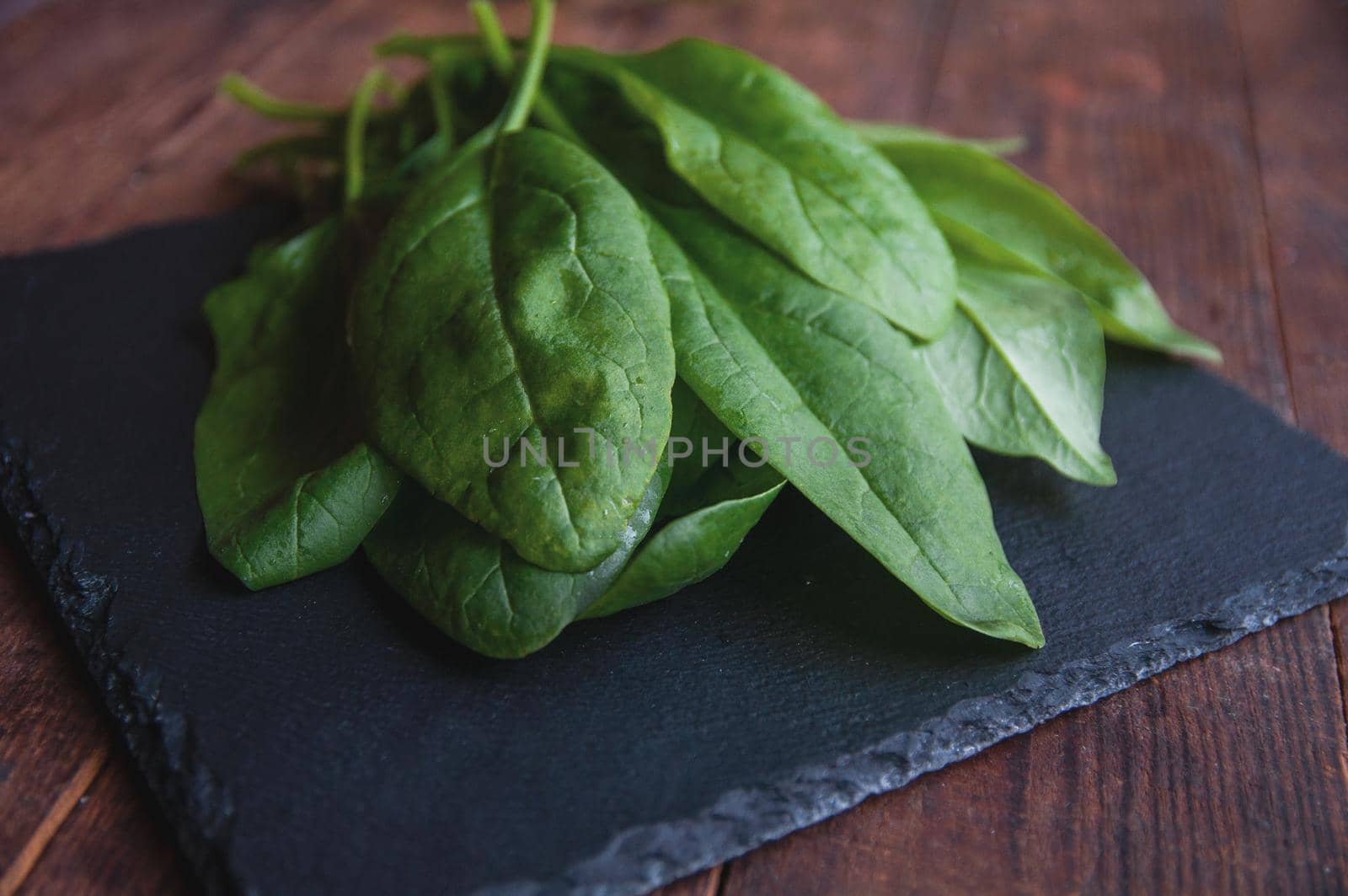 fresh spinach lies on a black presentation board located on a brown wooden table