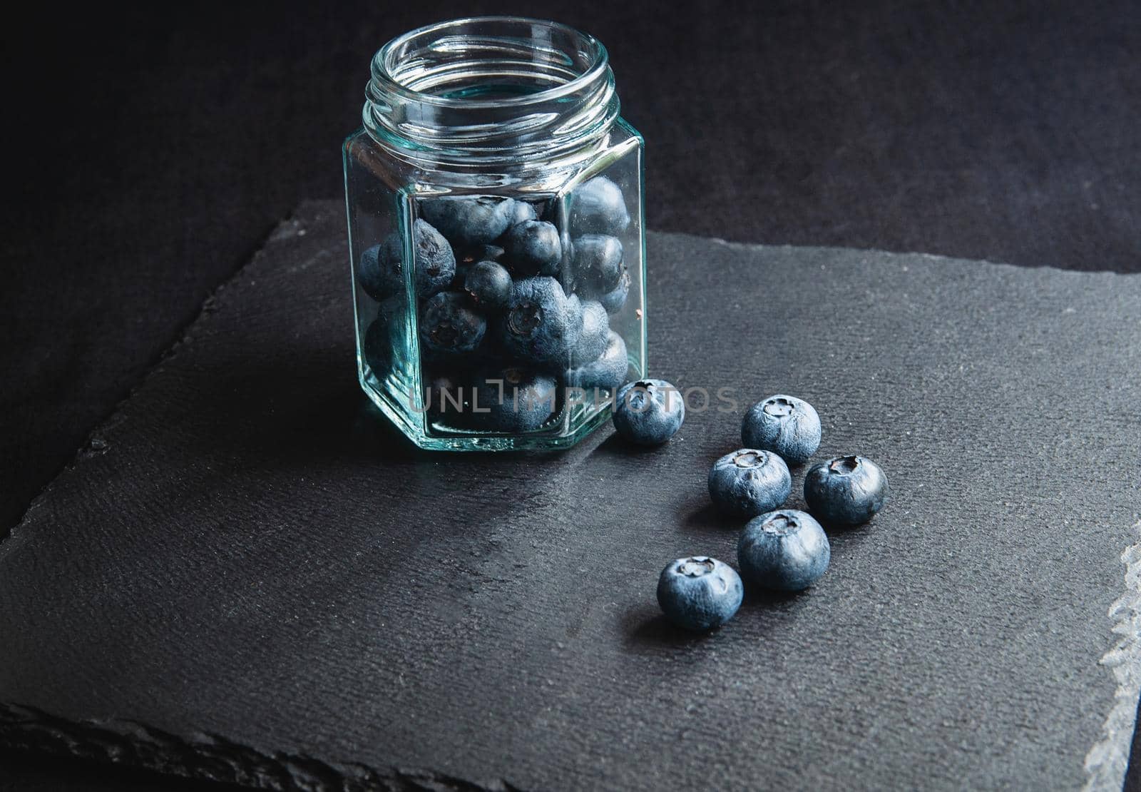 Fresh blueberries in a glass jar and laid out on a black board. by ozornina