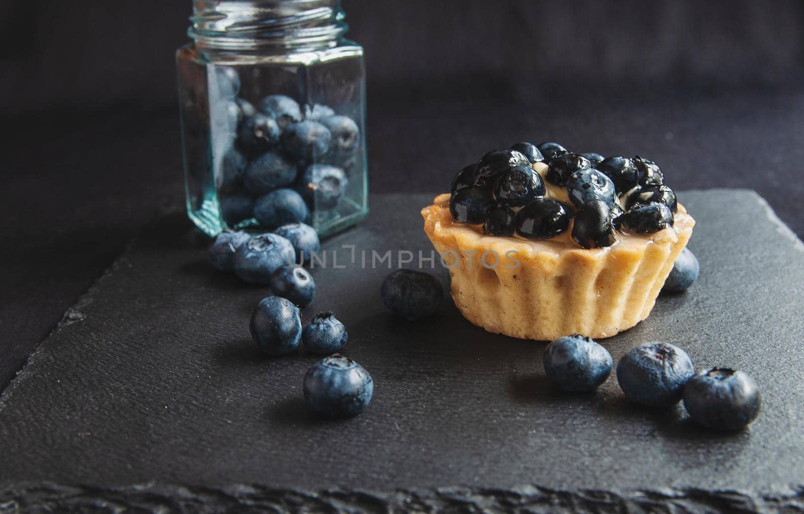 Blueberry cupcake on black serving board with scattered berries by ozornina
