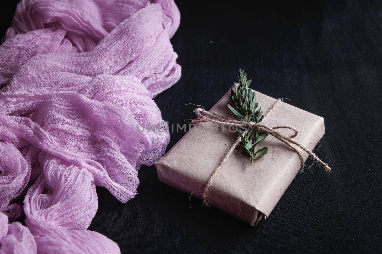 Kraft paper gift box next to a vintage tablecloth hand-painted with pink gauze on black background