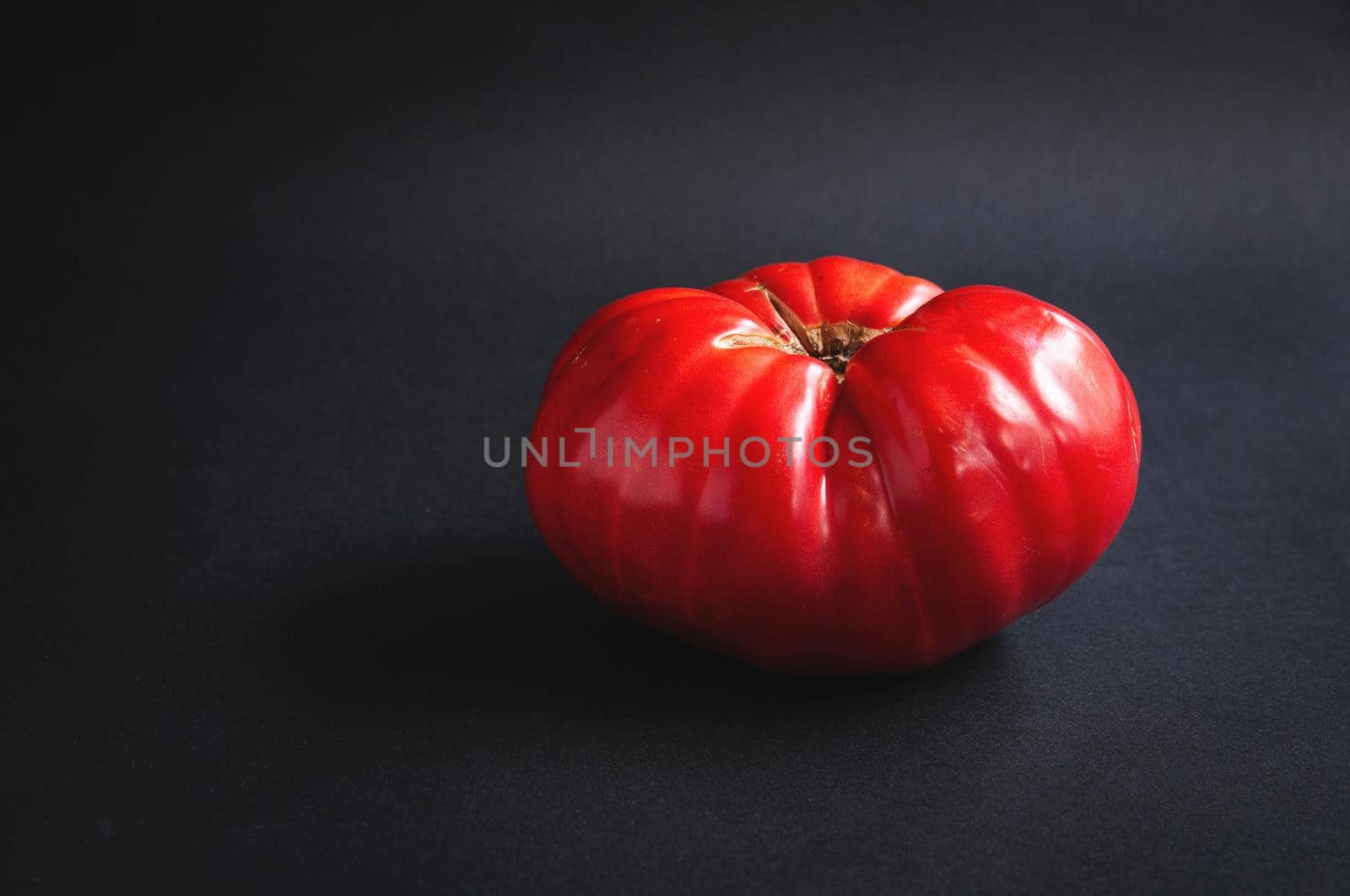 Huge big red tomato on a black serving board on a dark background
