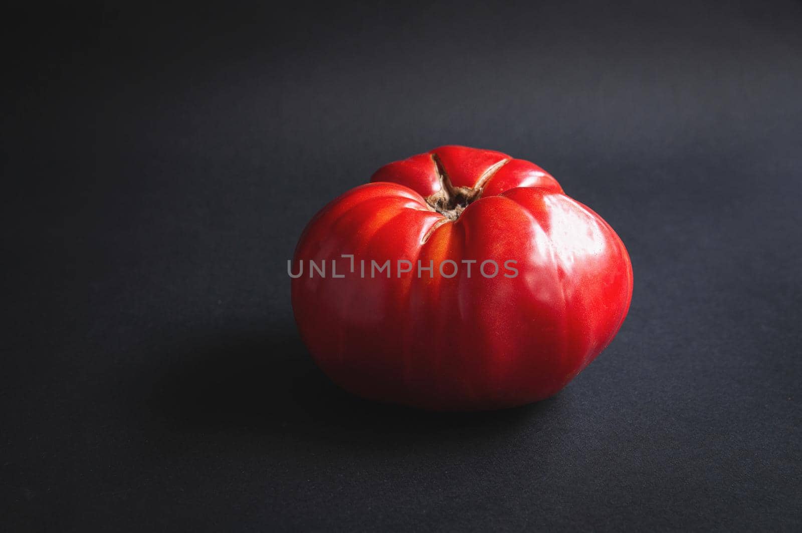 Huge big red tomato on a black serving board on a dark background