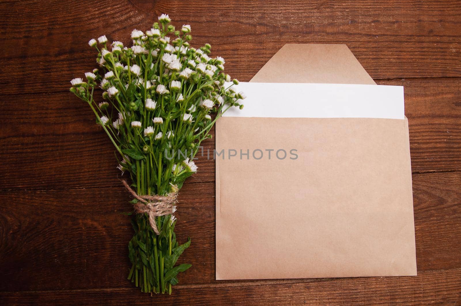 envelope made of craft paper, next to a bouquet of chamomile flowers, which lies on a wooden table