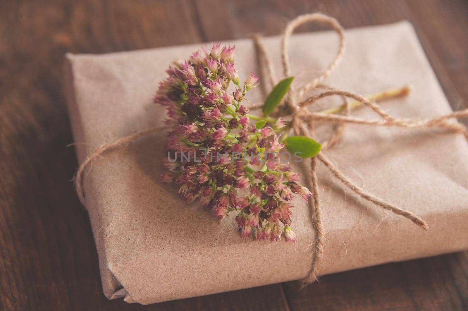 Homemade wrapped present in kraft paper and pink flowers on a wood table. by ozornina