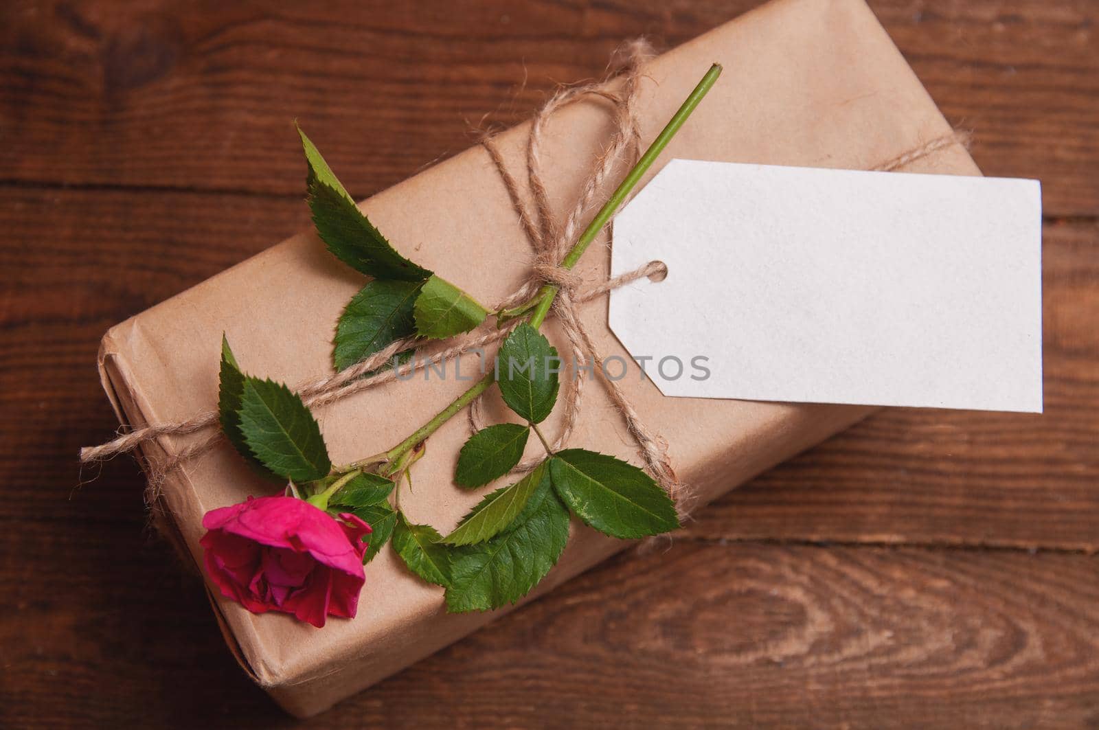 gift wrapped in craft paper on top of a flower rose tied with twine, which lies on a wooden table