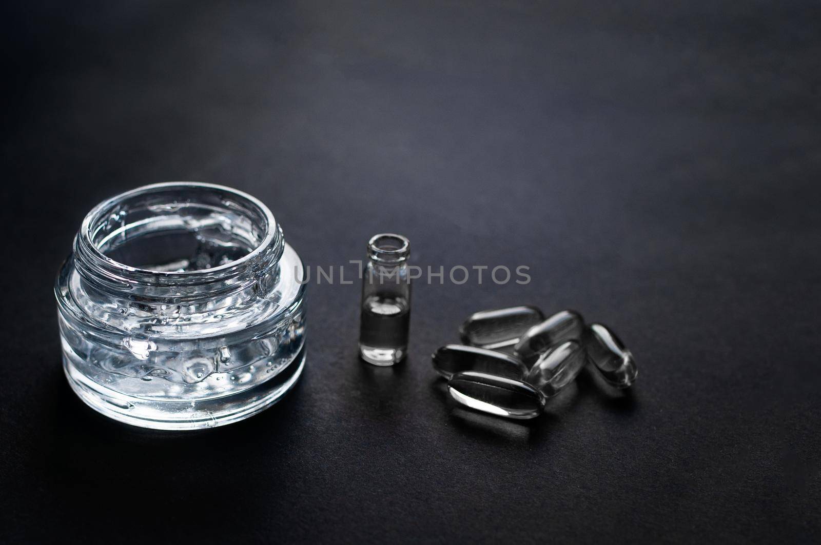 transparent jar with moisturizing gel with hyaluronic acid and vitamins in capsules on a black background