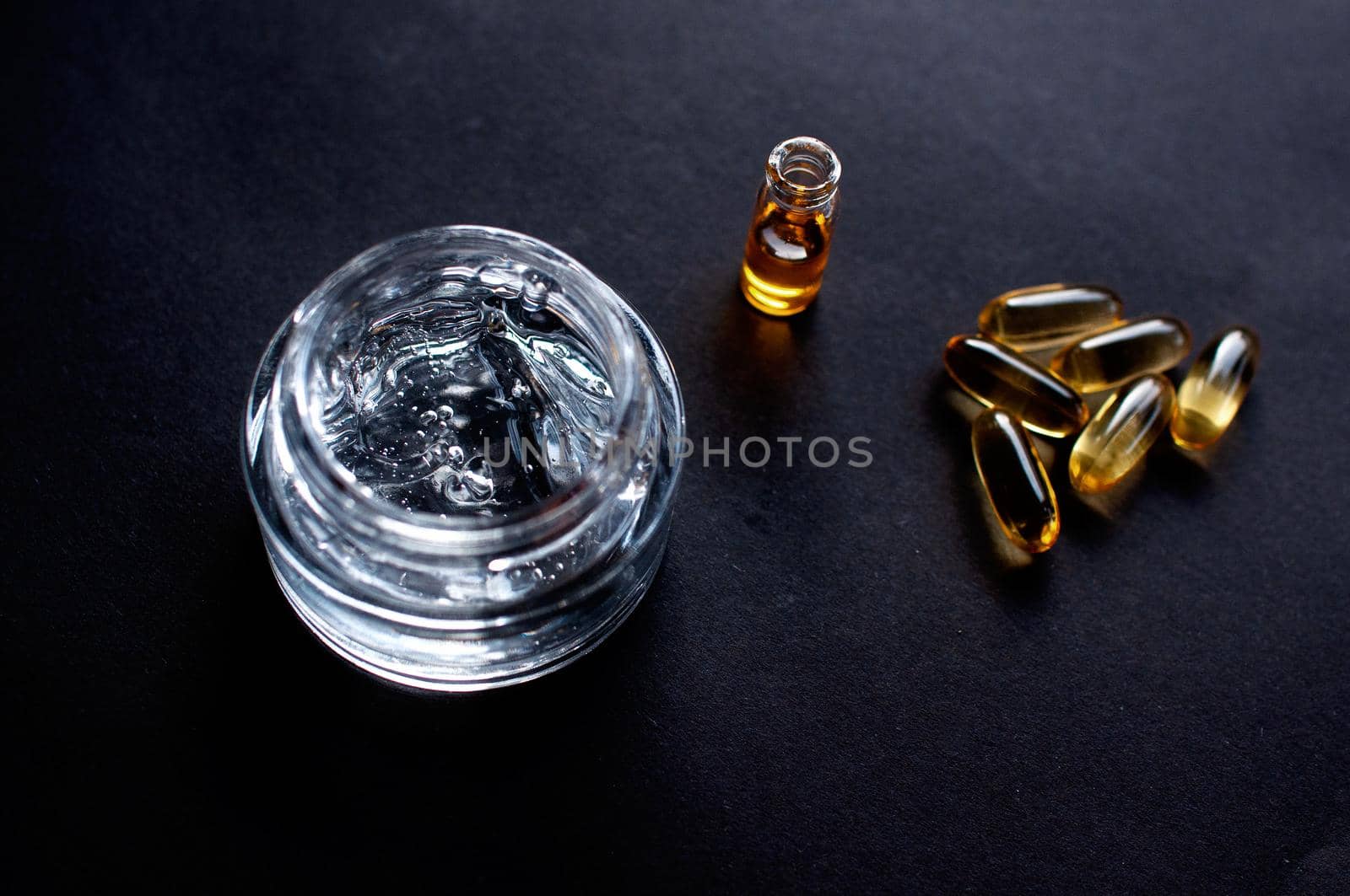 transparent jar with moisturizing cream with hyaluronic acid and vitamins in capsules on a black background